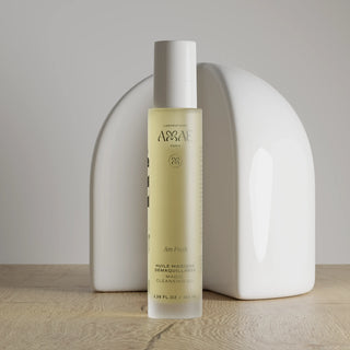 Flacon de l’huile magique démaquillante de Laboratoire Amaé, huile nettoyante visage présentée en packshot sur une table en bois avec une structure géométrique en arrière plan.